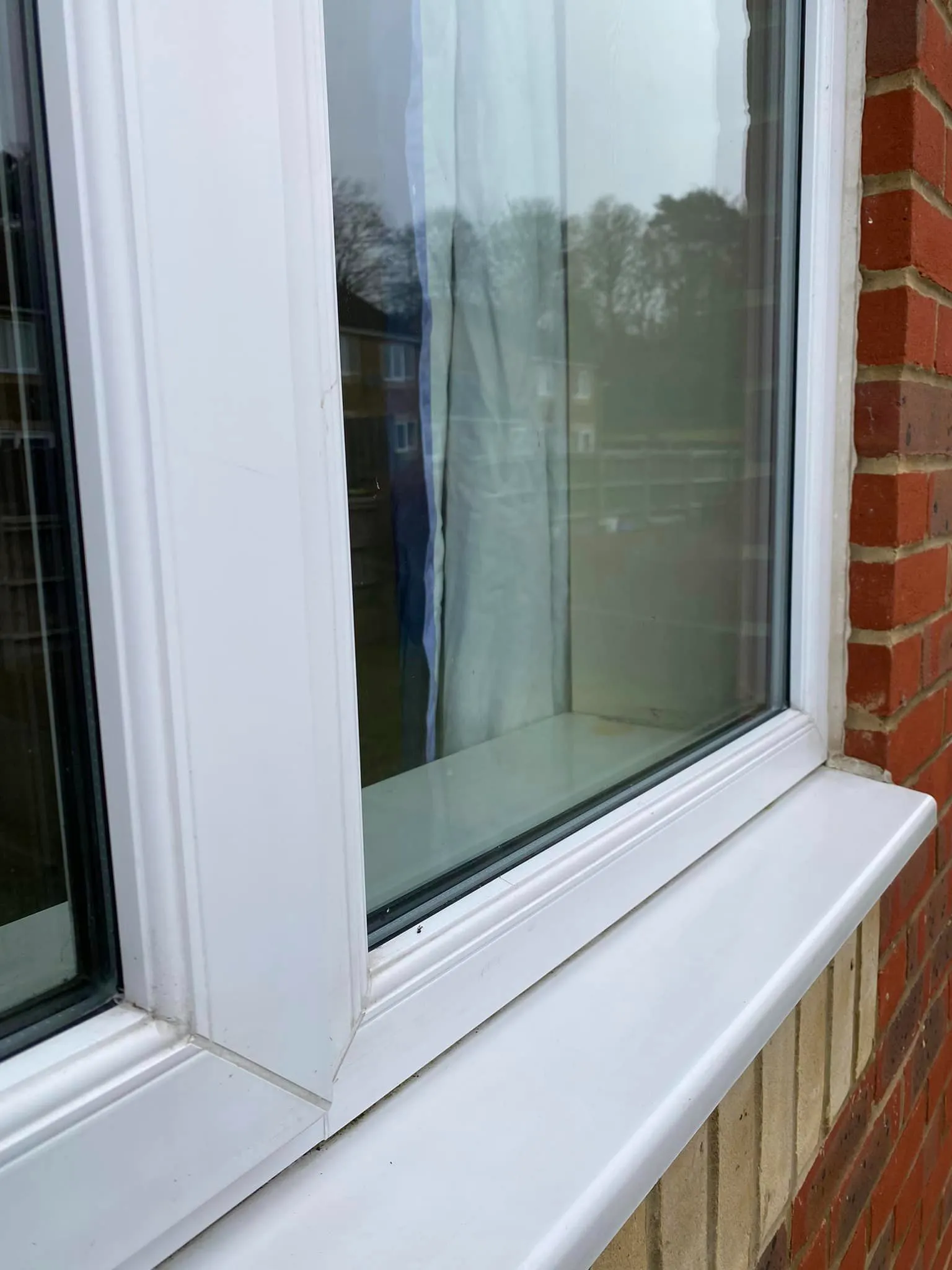 A cat sitting on a window sill next to a brick building.